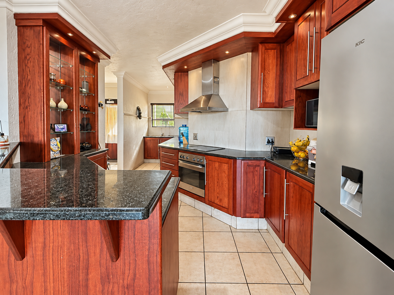 A well-maintained kitchen featuring rich wooden cabinetry, granite countertops, built-in stainless steel appliances, and integrated glass display shelving.