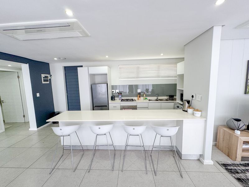 Modern open-plan kitchen featuring a sleek breakfast island, integrated appliances, gas hob, and contemporary finishes with neutral tiled flooring.