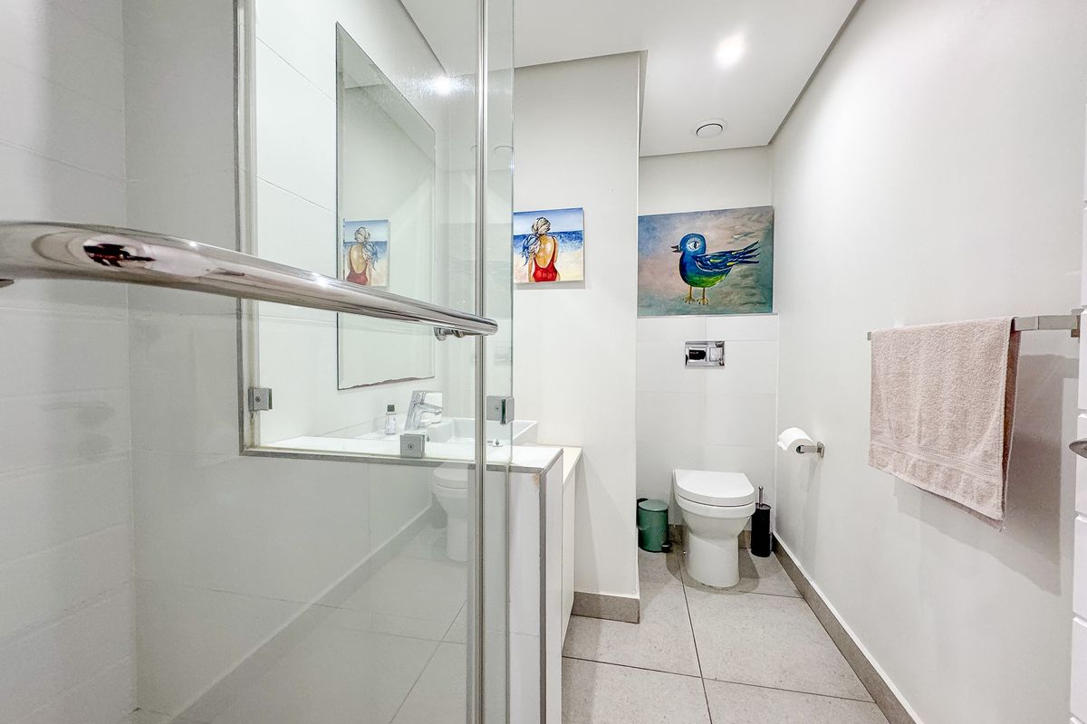 Modern bathroom featuring a glass-enclosed shower, wall-mounted toilet, and vanity basin with clean, neutral tiling throughout.