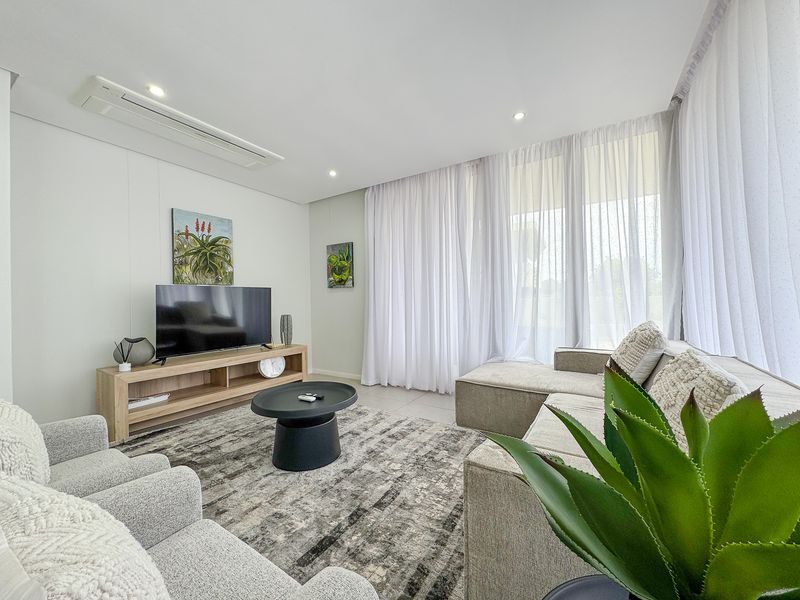 A bright and modern living room featuring tiled flooring, recessed downlighting, ducted air conditioning, and floor-to-ceiling sheer curtains.