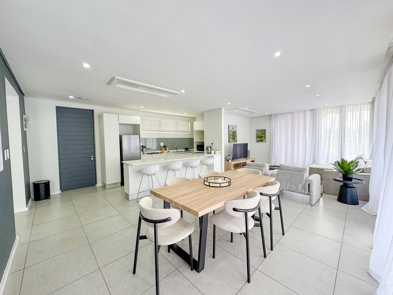 Spacious open-plan living area featuring a modern kitchen with island, tiled floors, and integrated lighting, seamlessly flowing into the dining and lounge space.