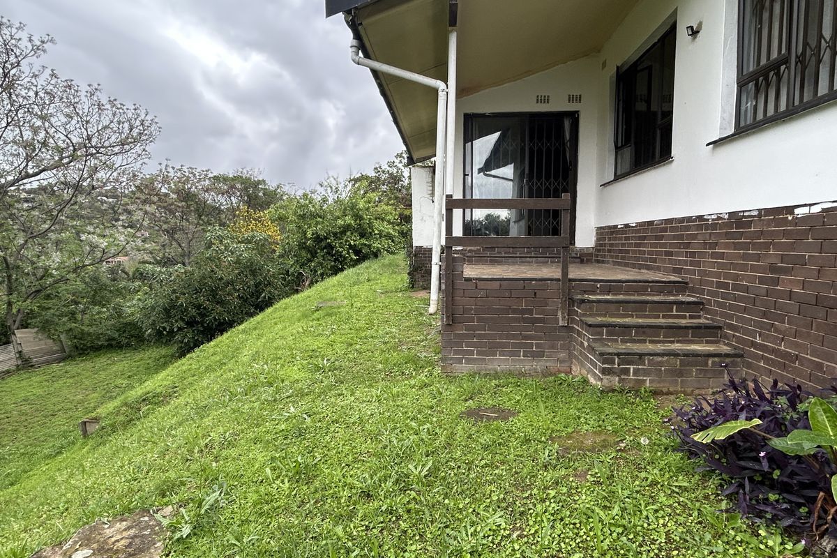 Rear exterior view of the house featuring a brick facade, a small raised patio area, and access to the sloped garden.