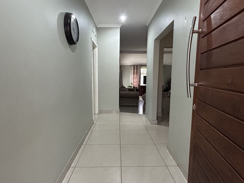 A bright, tiled hallway featuring a solid wooden front door and recessed lighting, providing a clean transition into the main living areas.