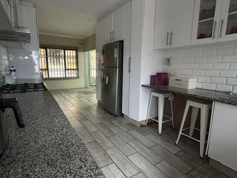 A functional kitchen featuring granite countertops, white cabinetry, subway tile backsplash, and ceramic floor tiles, with an adjacent open-plan living area.