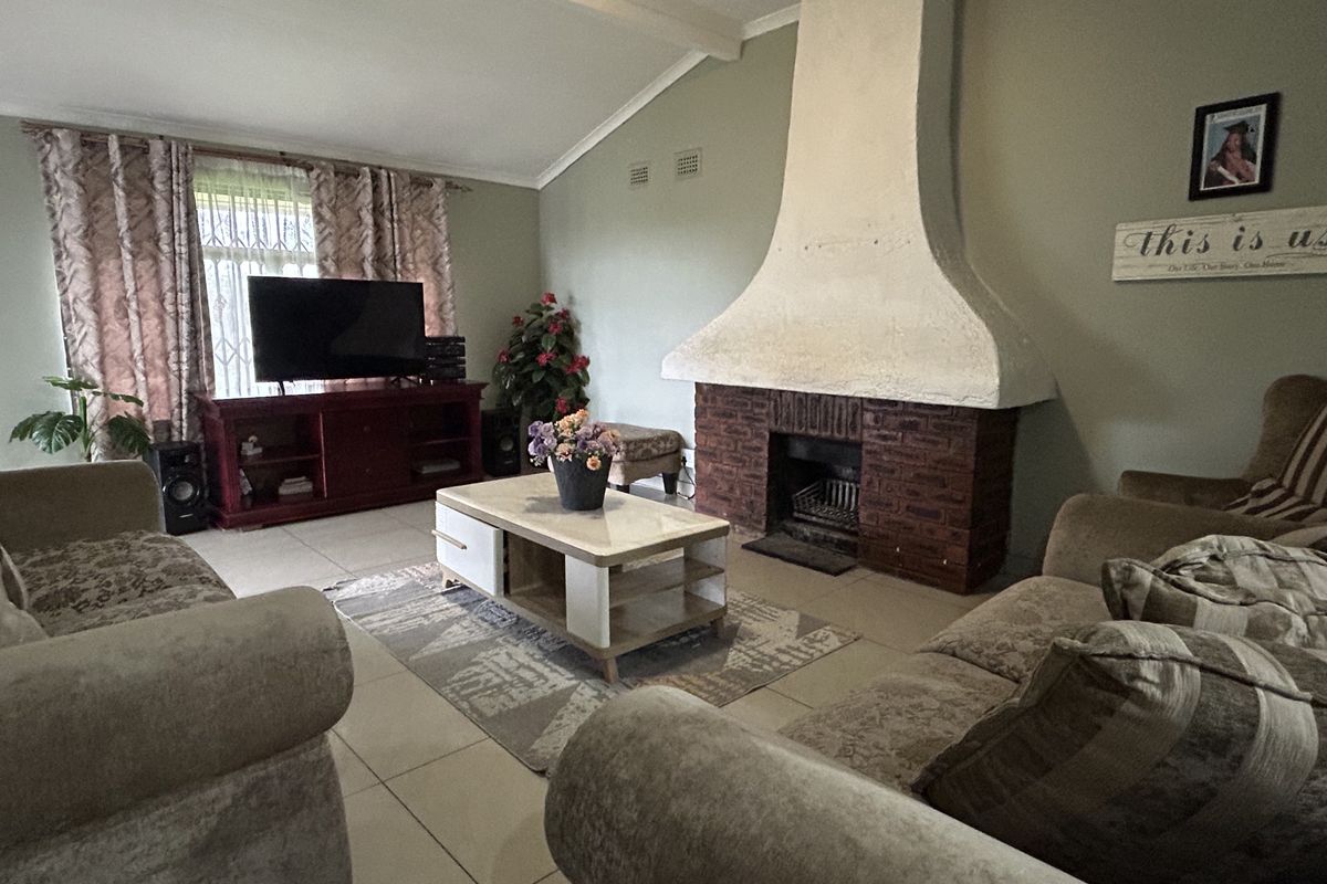 A living room featuring a prominent brick fireplace with a white chimney breast, vaulted ceilings, and tiled flooring.