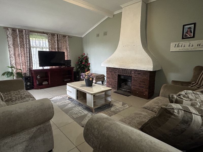 A living room featuring a prominent brick fireplace with a white chimney breast, vaulted ceilings, and tiled flooring.