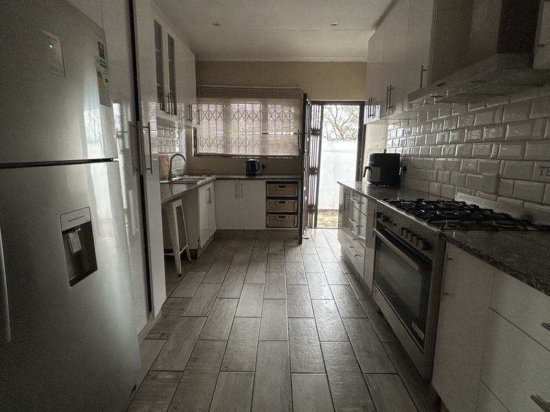 A functional galley-style kitchen featuring white cabinetry, granite countertops, subway tile backsplash, gas hob, and tiled flooring with direct access to the rear exterior.