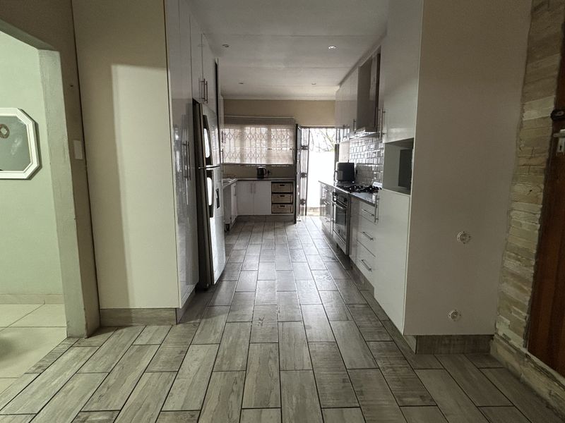 Modern galley-style kitchen featuring white cabinetry, subway tile backsplash, built-in oven and gas hob, and wood-look tiled flooring.