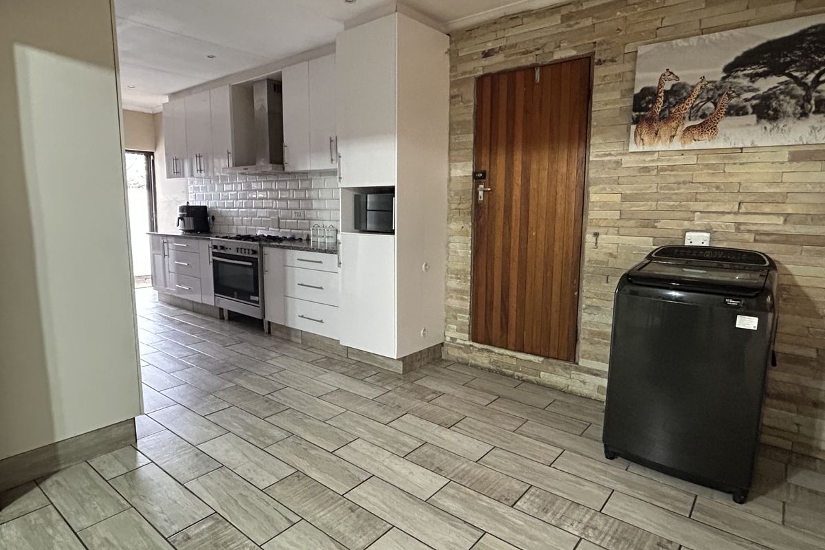 Modern kitchen featuring white cabinetry, stone tile backsplash, built-in oven and hob, complemented by a textured stone feature wall and tiled flooring.