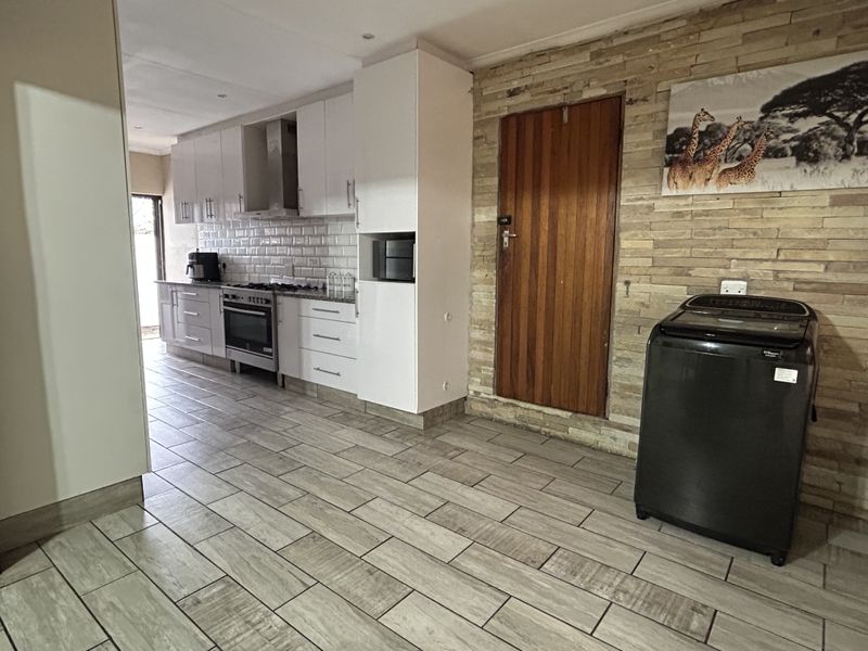 Modern kitchen featuring white cabinetry, stone tile backsplash, built-in oven and hob, complemented by a textured stone feature wall and tiled flooring.