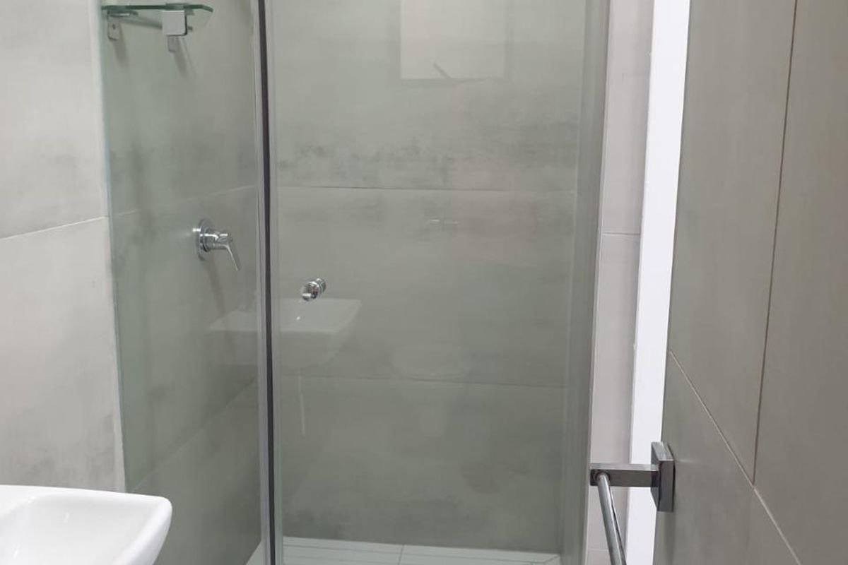 Modern bathroom featuring a glass-enclosed shower, wall-mounted basin, and neutral large-format wall and floor tiles.