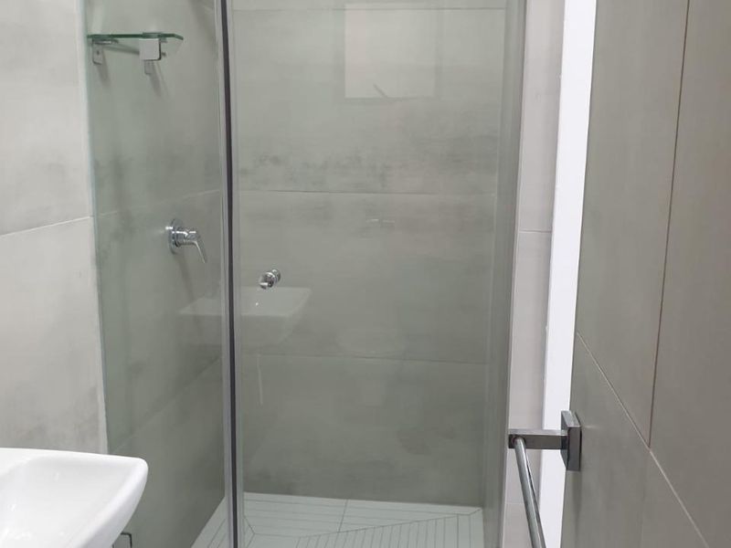 Modern bathroom featuring a glass-enclosed shower, wall-mounted basin, and neutral large-format wall and floor tiles.