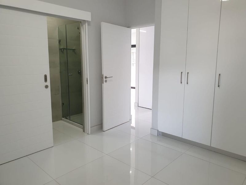 Modern bedroom featuring high-gloss built-in cupboards, polished tiled flooring, and direct access to a contemporary en-suite bathroom with a glass shower enclosure.