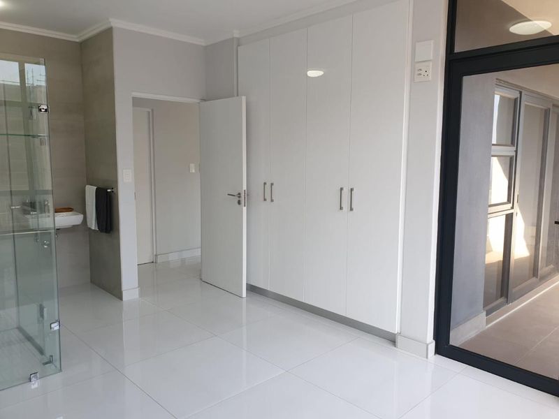 Modern bedroom featuring sleek white built-in cupboards, polished tiled flooring, and an en-suite glass shower enclosure with direct access to a balcony.