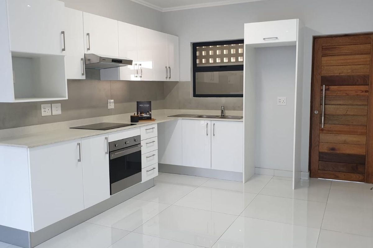 Modern kitchen featuring white high-gloss cabinetry, stone countertops, integrated oven and hob, and polished tiled flooring in a clean, contemporary space.