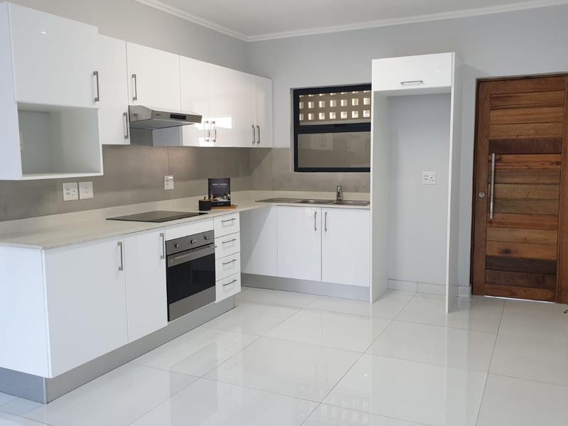 Modern kitchen featuring white high-gloss cabinetry, stone countertops, integrated oven and hob, and polished tiled flooring in a clean, contemporary space.
