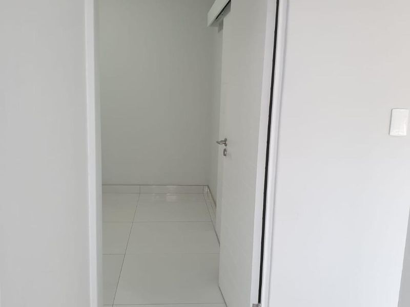 A clean, empty hallway featuring white tiled flooring and a white internal door, presenting a neutral and well-maintained transition space.