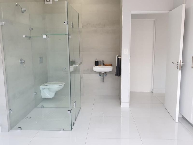 Modern bathroom featuring a wall-mounted toilet, glass-enclosed shower, and wall-mounted basin with clean, neutral tiling throughout.
