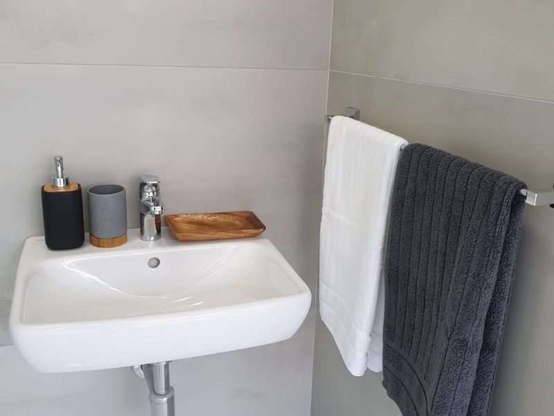 A modern bathroom featuring a sleek wall-mounted basin with chrome fixtures and large format neutral wall tiles.