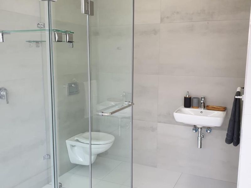 Modern bathroom featuring a glass-enclosed shower, wall-mounted basin, and wall-hung toilet with neutral large-format tiling throughout.