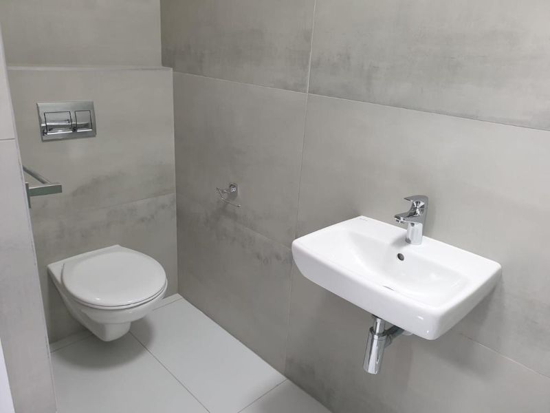 Modern guest bathroom featuring a wall-mounted toilet with concealed cistern and a sleek wall-mounted basin with chrome fixtures, finished with large format neutral tiles.