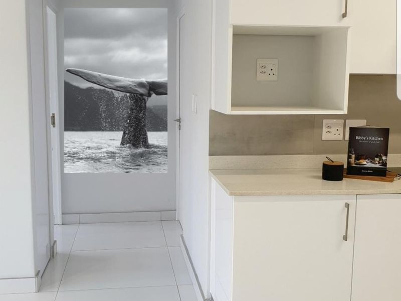 A modern, minimalist kitchen area featuring sleek white cabinetry, stone countertops, and polished tiled flooring, presenting a clean and contemporary aesthetic.