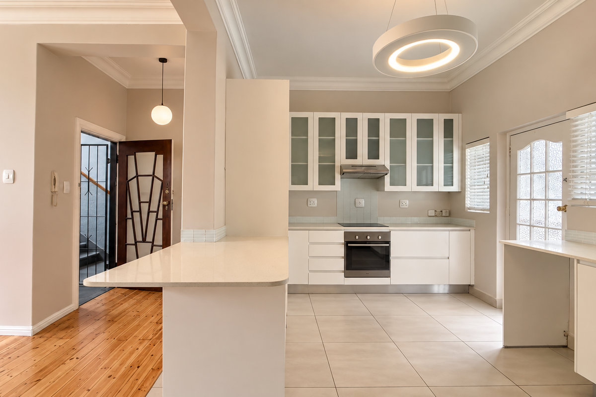 Modern kitchen featuring white cabinetry, stone countertops, integrated appliances, and a seamless transition between tiled and timber flooring.