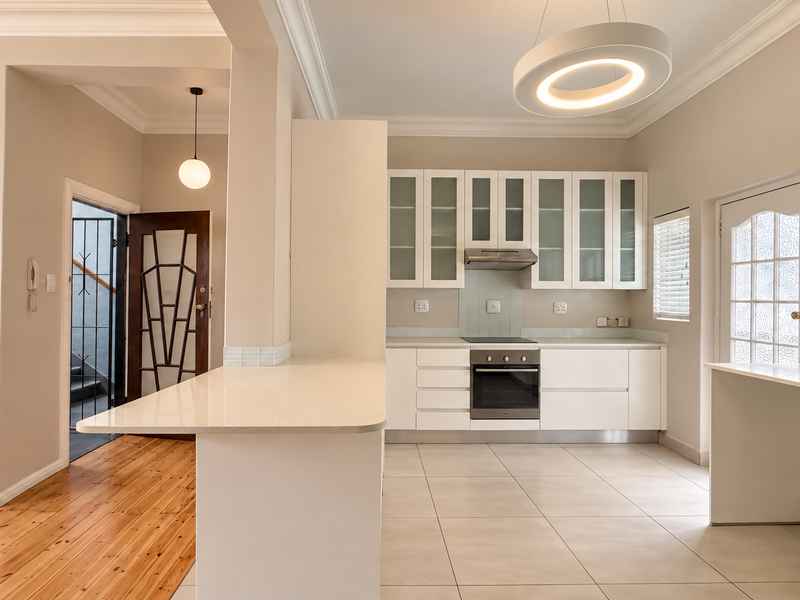 Modern kitchen featuring white cabinetry, stone countertops, integrated appliances, and a seamless transition between tiled and timber flooring.