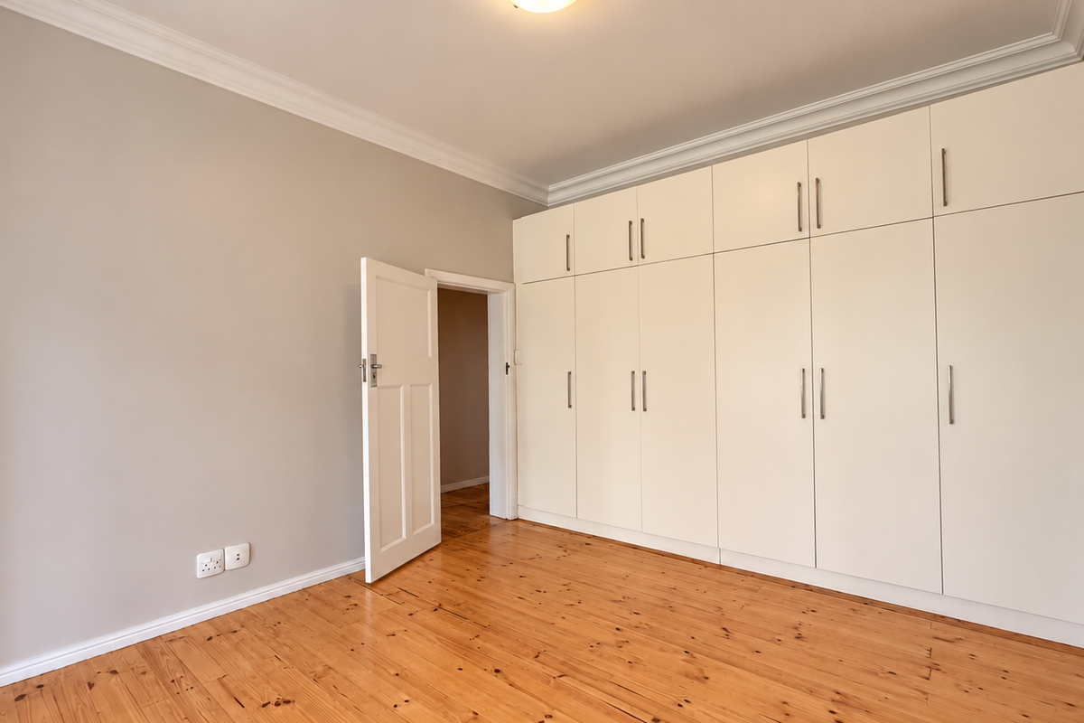 A bright, empty bedroom featuring polished timber flooring, neutral walls, and extensive floor-to-ceiling built-in cabinetry with ample storage space.