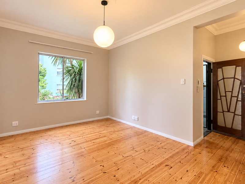A bright and spacious living area featuring polished timber flooring, decorative cornices, and a characterful timber-framed glass door.