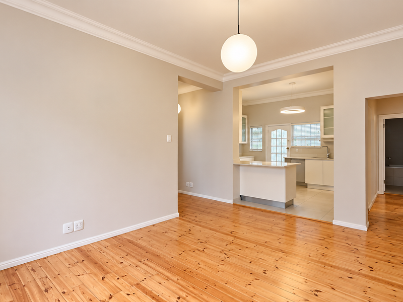 Spacious open-plan living area featuring polished timber flooring, crown molding, and a seamless transition into a functional kitchen with modern cabinetry.