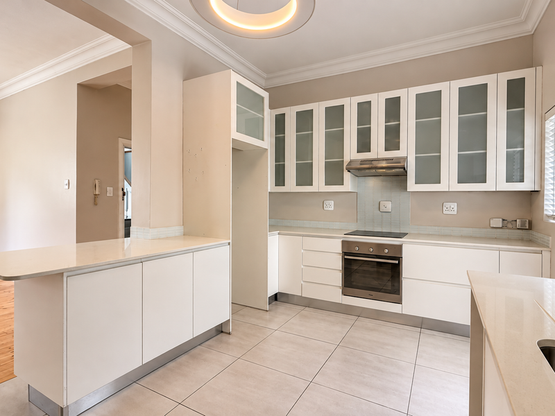 Modern kitchen featuring white cabinetry, stone countertops, integrated oven and hob, and tiled flooring, with an open-plan layout connecting to the living area.
