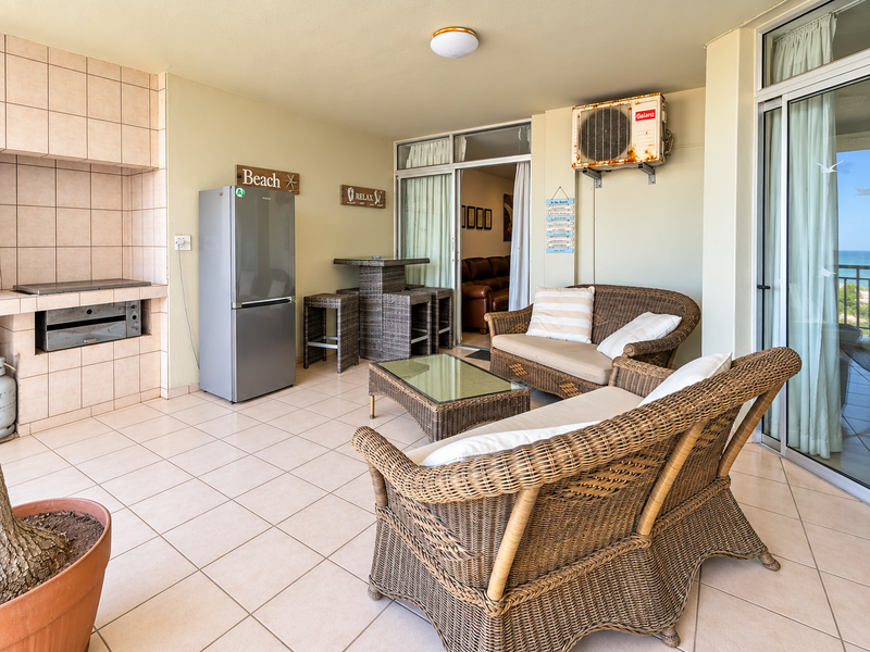 Covered balcony featuring a built-in braai, tiled flooring, and sliding glass doors, providing an outdoor entertainment space with ocean views.
