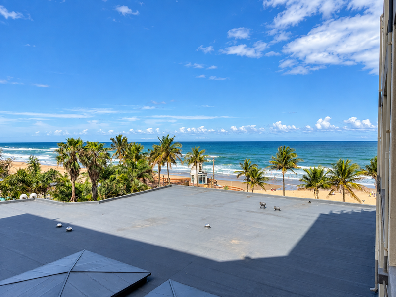Elevated view overlooking the coastline, beach, and ocean, featuring a flat roof structure with integrated skylights in the foreground.