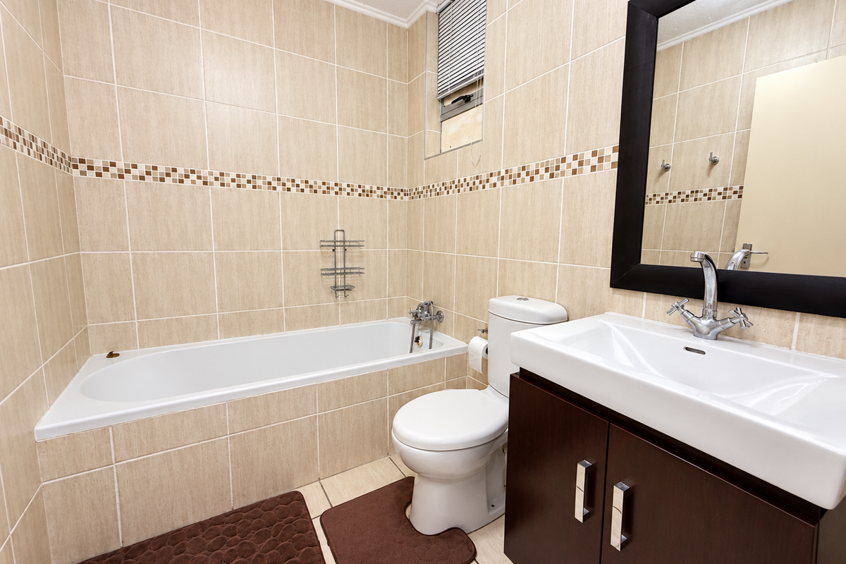A functional bathroom featuring a bathtub, toilet, and a dark wood vanity cabinet with a basin, finished with neutral wall and floor tiling.