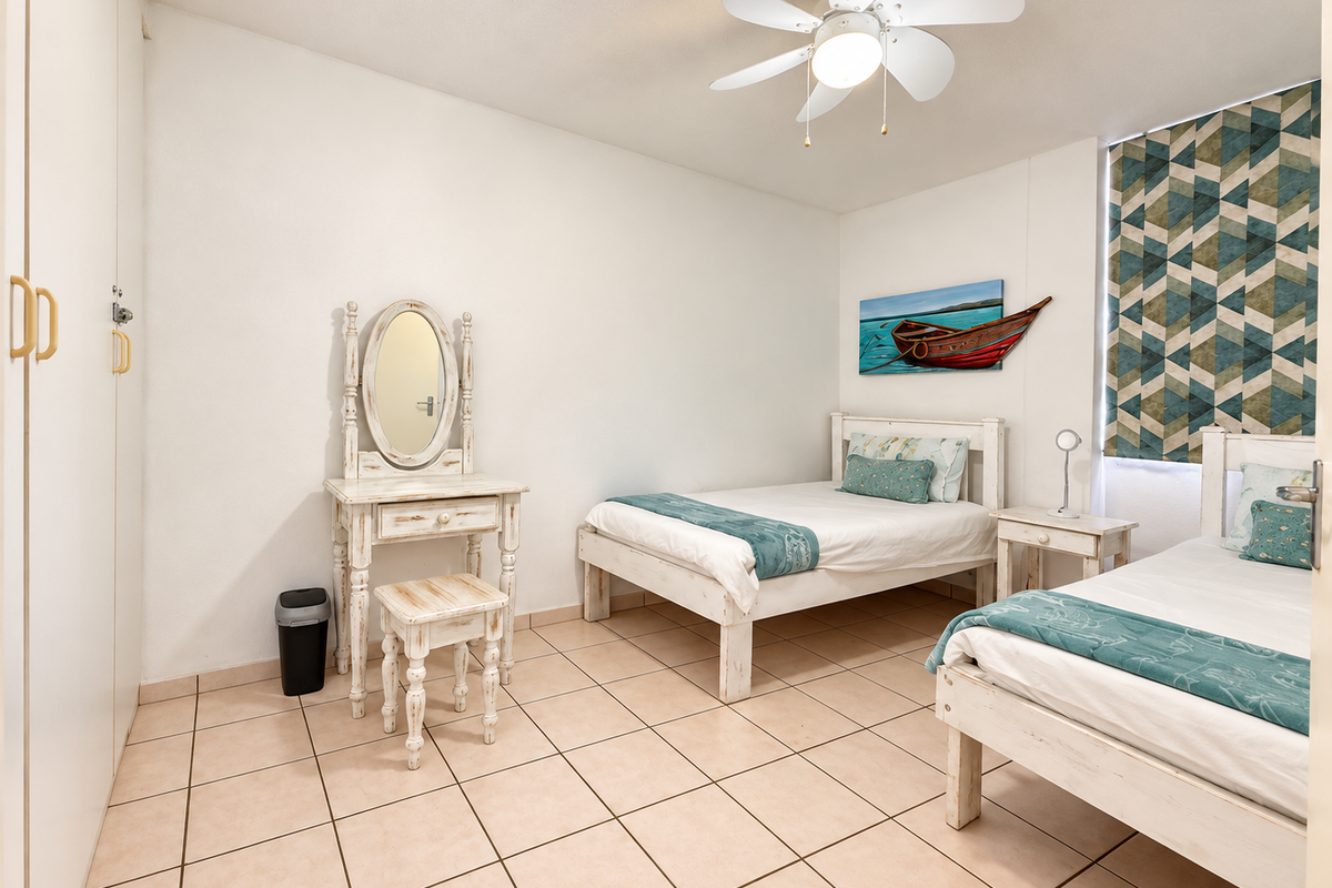 A bedroom featuring tiled flooring, built-in cupboards, and a ceiling fan, offering a functional and well-maintained living space.