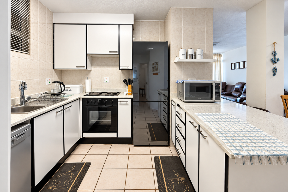A functional kitchen featuring white cabinetry with black trim, stone countertops, a built-in oven, and a breakfast bar overlooking the living area.