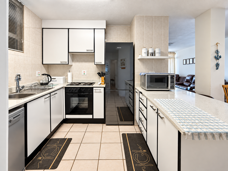 A functional kitchen featuring white cabinetry with black trim, stone countertops, a built-in oven, and a breakfast bar overlooking the living area.