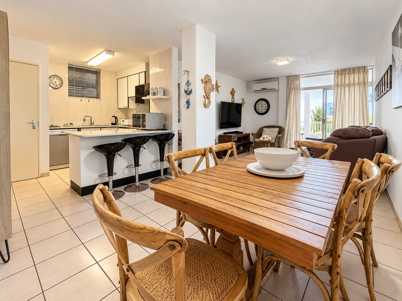 Open-plan living and dining area featuring tiled floors, a functional kitchen with island seating, and direct access to a private balcony.