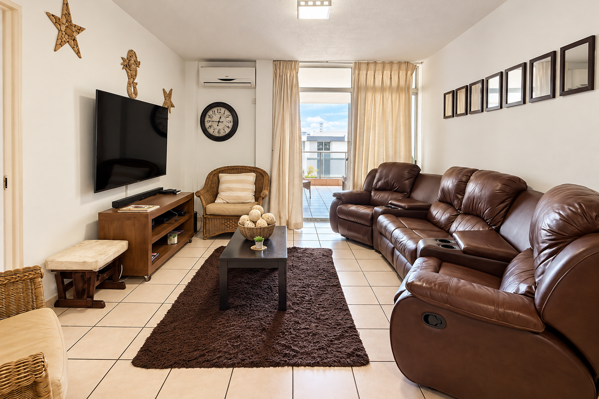 A comfortable living room featuring tiled flooring, a wall-mounted air conditioning unit, and direct access to an outdoor balcony through sliding glass doors.