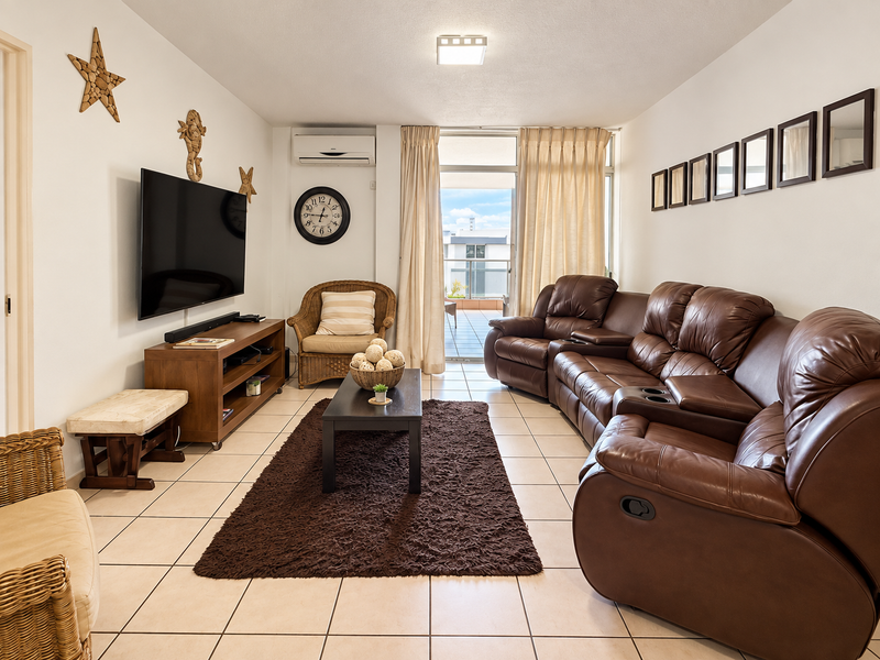 A comfortable living room featuring tiled flooring, a wall-mounted air conditioning unit, and direct access to an outdoor balcony through sliding glass doors.