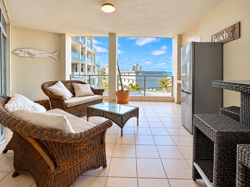 Spacious covered balcony featuring tiled flooring, a glass balustrade, and a built-in counter area, offering an open-air living space with coastal views.