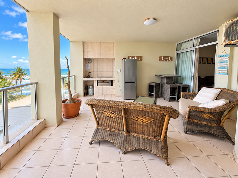 Spacious covered balcony featuring a built-in braai, tiled flooring, and a glass balustrade with scenic ocean views.