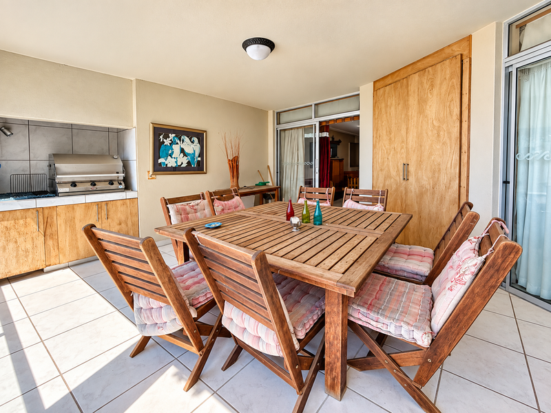 Covered patio area featuring tiled flooring, a built-in braai with cabinetry, and sliding glass door access to the interior living space.