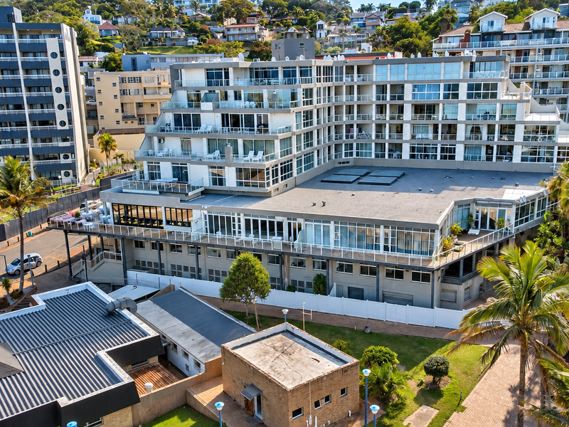 Aerial view of a multi-story apartment complex featuring tiered balconies, large glass facades, and a paved ground-level courtyard area.