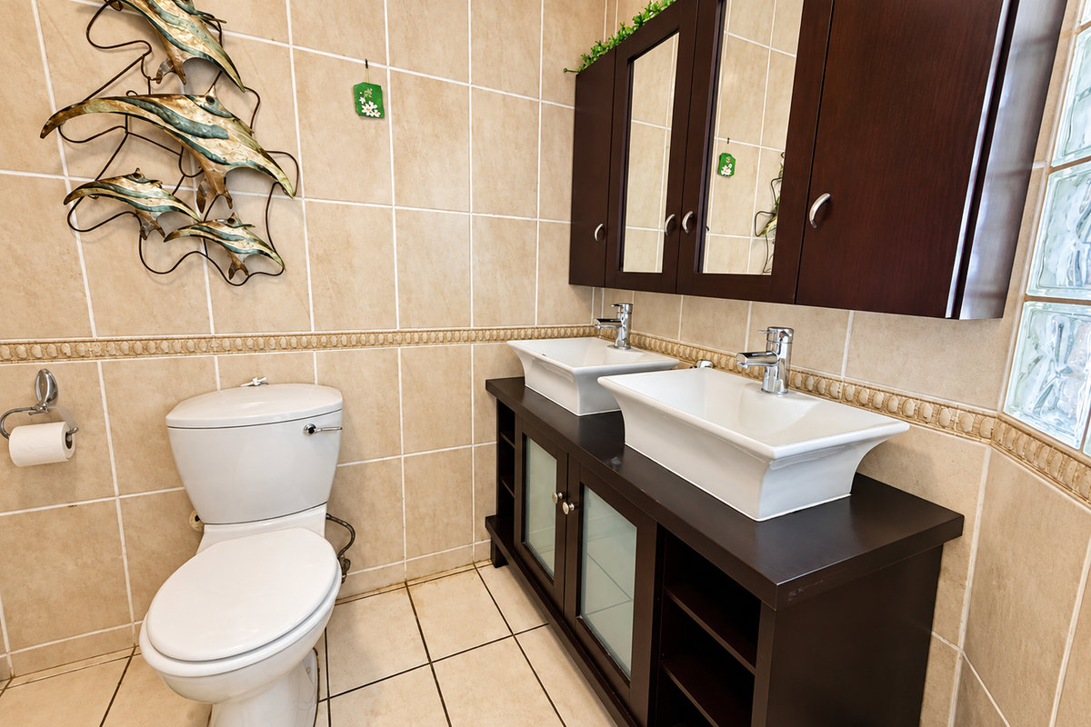 A well-maintained bathroom featuring a double vanity with vessel sinks, dark wood cabinetry, wall-mounted medicine cabinets, and neutral ceramic tiling throughout.