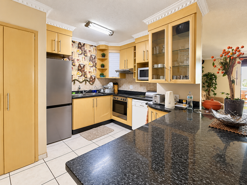 A functional kitchen featuring light wood cabinetry, dark granite countertops, built-in appliances, and tiled flooring with crown molding details.