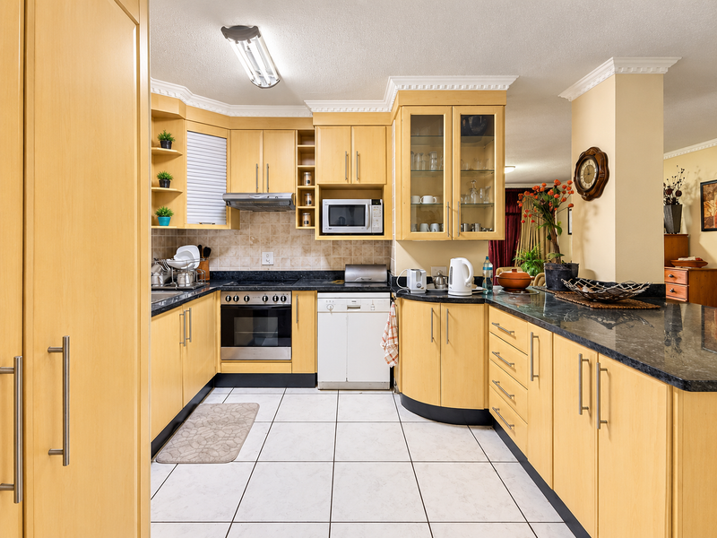 A functional kitchen featuring light wood cabinetry, granite countertops, built-in appliances, and tiled flooring with a breakfast bar area.