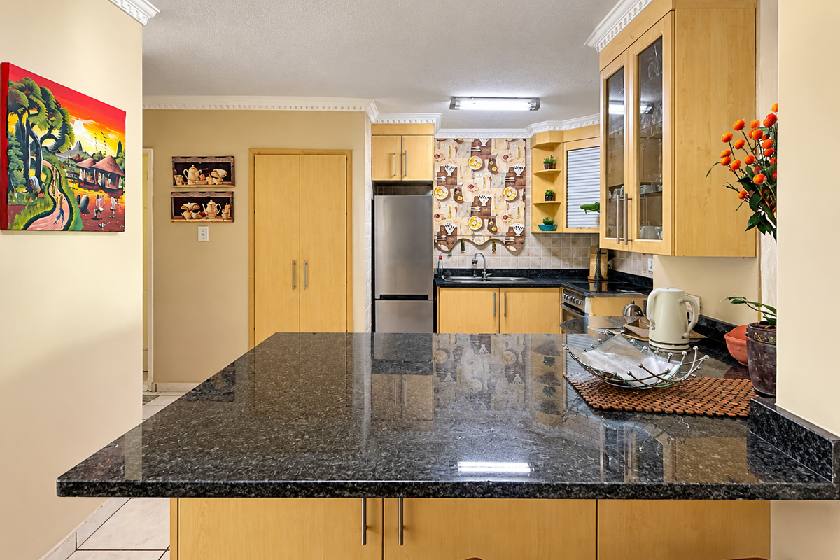 A functional kitchen featuring light wood cabinetry, dark granite countertops, and a breakfast bar, complemented by crown molding and neutral wall finishes.