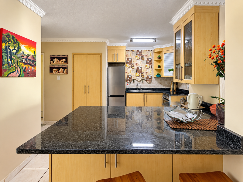 A functional kitchen featuring light wood cabinetry, dark granite countertops, and a breakfast bar, complemented by crown molding and neutral wall finishes.